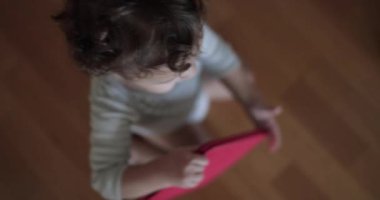 Bir erkek bebek, bir tableti merakla kavrar. Meraklı gözleri, cihazı sunarken yukarı bakar..