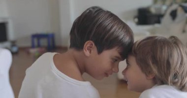 İki küçük çocuk, içeride eğleniyorlar. Gözleri dostça bakan bir yarışmaya kilitleniyorlar. Arka planda oyuncaklar var..