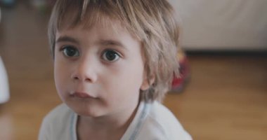 Merak ve merakın ifadesini gösteren genç bir çocuğun yakın çekimi, bulanık bir arka plan ile bir ev ortamını işaret ediyor..