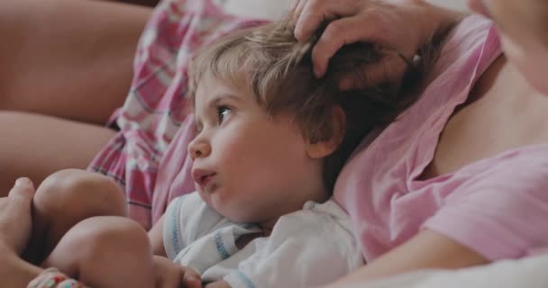 一位母亲轻轻地抚摩着她年幼的儿子们的头发 他们共享着宁静的时光 孩子仰起头 舒服地靠在她身边 — 图库视频影像