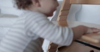 Küçük çocuk gün boyunca tahta bir sandalyeye tırmanmaya çalışıyor, merak ve bağımsızlık anını yakalıyor..