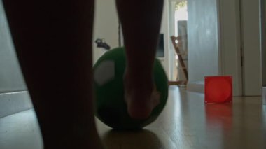 Bir çocuğun düşük açılı görüntüsü, oturma odasında yeşil bir futbol topuyla oynarken dikkatle odaklanarak oyuna olan sevgisini gösteriyor..