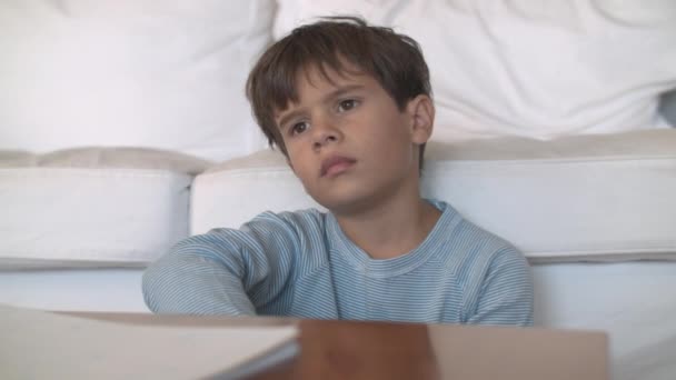 Young Boy Blue Pajamas Sits Contemplative Expression White Cushioned Couch — Stock Video