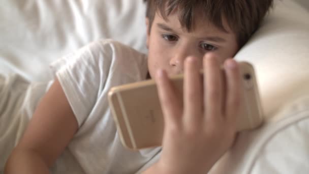 Chłopiec Brązowymi Włosami Skupia Się Smartfonie Leżącym Białej Kanapie — Wideo stockowe
