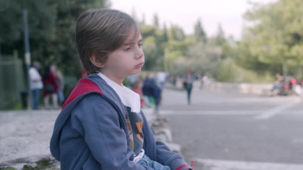 Ένα Νεαρό Αγόρι Κάθεται Στην Άκρη Του Πεζοδρομίου Έξω Κοιτάζοντας — Αρχείο Βίντεο
