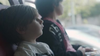 Kulaklıklı düşünceli genç bir çocuk hareket halindeki bir otobüsün penceresinde oturur ve düşünceli bir ifadeyle dışarıya bakar..