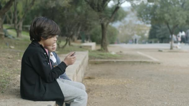 Młody Chłopak Smartfonem Siedzi Ławce Parku Pozornie Rozmawiając Kimś Obok — Wideo stockowe