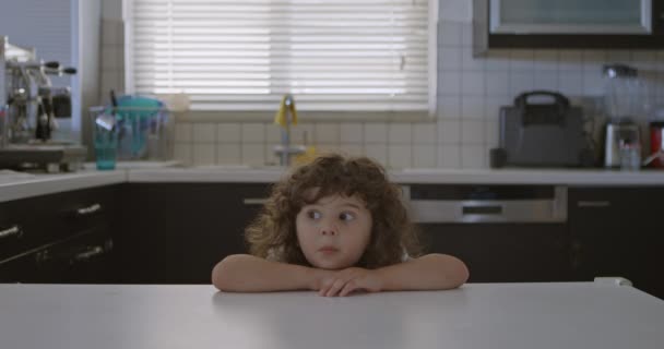 Kędzierzawy Chłopiec Kładzie Podbródek Rękach Przy Blacie Kuchennym Jego Oczy — Wideo stockowe