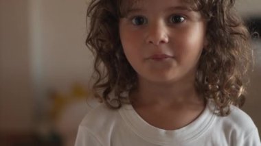 Uzun, kıvırcık bukleli neşeli bir çocuk, kollarını uzatarak, çocukluk masumiyeti ve hayal gücünün özünü yakalamak için kamerayla oynaşıyor..