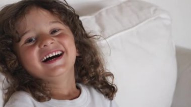 Uzun, kıvırcık bukleli neşeli bir çocuk, kollarını uzatarak, çocukluk masumiyeti ve hayal gücünün özünü yakalamak için kamerayla oynaşıyor..