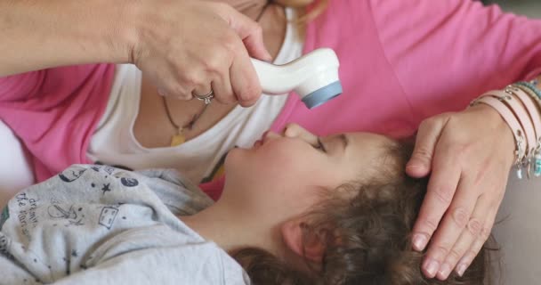 一个孩子躺在床上 而一个关心的母亲则轻轻地用额头温度计检查发烧情况 这表明她正在接受家庭医疗护理 — 图库视频影像
