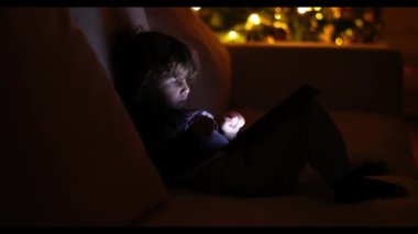 Küçük bir çocuk bilgisayar ekranının önünde oturuyor, dijital tabletle etkileşime girerken odaklanmış ve meşgul..