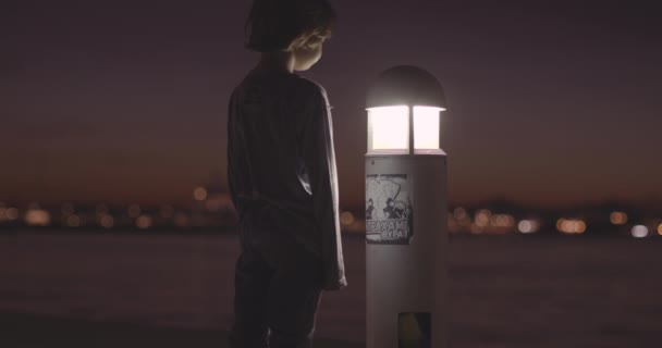 Ragazzo Solitario Trova Accanto Lampione Incandescente Crepuscolo Con Luci Lontano — Video Stock