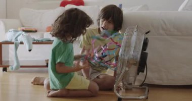 İki genç çocuk ellerinde renkli kağıt parçalarıyla evde oturmuş gülüyor ve rüzgarın yarattığı hareketin tadını çıkarıyorlar..