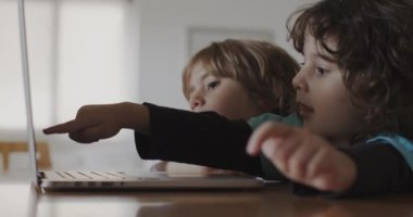 İki küçük çocuk bir dizüstü bilgisayar ekranına odaklanıyor, bir çocuk ilginç bir şeyi işaret ediyor, bir keşif anını paylaşıyor ve oturma odalarında öğreniyor..