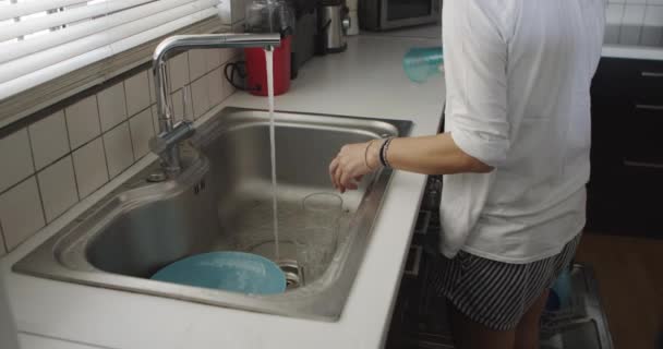 一个女人站在厨房的水池边 用水龙头里的水冲洗蓝色的盘子 — 图库视频影像