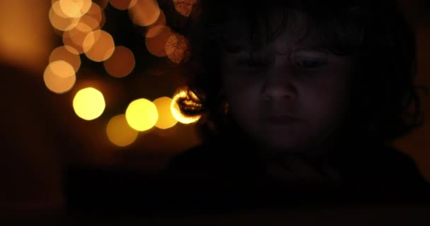 一个小男孩躺在床上 被数字平板电脑的明亮屏幕所吸引 背景中闪烁着柔和的微光 — 图库视频影像