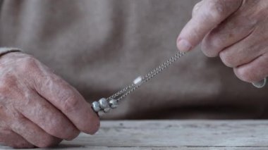 Yaşlı bir adam, elleri yıpranmış gümüş bir zinciri kavrıyor ve her ikisinin de karmaşık detaylarını ve dokularını gösteriyor..