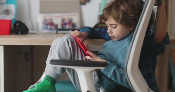 2人の小さな少年がデジタルタブレットに焦点を当てながら密接に座り 子供の寝室を示す背景にはおもちゃと本棚がありました — ストック動画