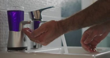Lavaboya ulaşmak için taburede duran adam ellerini sabun ve suyla temizce yıkıyor..