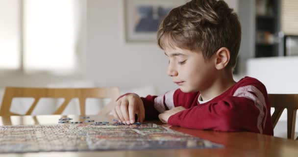 屋内の木のテーブルに活気に満ちたジグソーパズルを組み合わせ 問題解決のスキルを披露することに焦点を当てた少年 — ストック動画