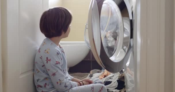 패턴이 잠옷을 소년은 독립과 책임감을 보여주는 프론트 세탁기에 신중하게 배치하고 — 비디오