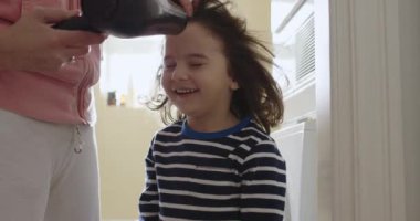 Bir anne, oğlunun saçını saç kurutma makinesiyle kurutuyor. Saçlarının uçuşmasına ve yüzünde neşeli bir ifade oluşmasına neden oluyor..