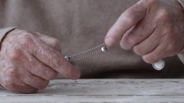 Yaşlı bir adam, elleri yıpranmış gümüş bir zinciri kavrıyor ve her ikisinin de karmaşık detaylarını ve dokularını gösteriyor..