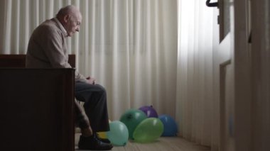 Yaşlı bir beyefendi, canlı balonlarla çevrili bir radyonun yanındaki bir yatakta düşünceli bir şekilde oturur. Kutlama ve yalnızlığın yan yana geldiğini öne sürerler..