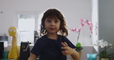 Kıvırcık saçlı tatlı çocuk mutfak lavabosunun üzerine eğilip musluktan su içiyor. Gün ışığı sahneyi aydınlatıyor..