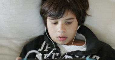 Kulaklık takan sevimli bir çocuk el bilgisayarı kumarı konsolunda oyun oynuyor. İçerideki bir kanepede rahatça yaslanıyor. Gün ışığında..