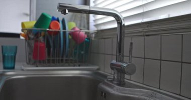 Bir mutfak lavabosunun üzerine modern paslanmaz çelik bir musluktan temiz mavi bir bardağa su döken adamların ellerini kapat, saksıların yanına..