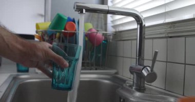 Bir mutfak lavabosunun üzerine modern paslanmaz çelik bir musluktan temiz mavi bir bardağa su döken adamların ellerini kapat, saksıların yanına..