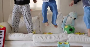 Üç çocuk dağınık oyuncak ve yastıklarla çevrili dağınık bir kanepenin üzerine atlarken yakalandı. Canlı bir iç seansın ortasında neşeli bir kaos hissi uyandırıyordu..