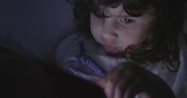 Genç bir çocuk beyaz bir kanepede rahatça oturur. Dikkatini, sakin alacakaranlık saatlerinde elinde tuttuğu kırmızı tablet çeker..