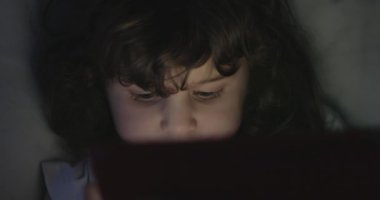 Bir çocuğun, gece odaklanmış gözlerine yansıyan dijital tablet ekranın yumuşak parıltısıyla aydınlanan yakın çekim görüntüsü..