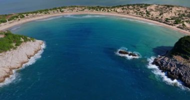 Voidokilia Sahili 'nin sakin kıvrımları yukarıdan çekiliyor, turkuaz berrak suların altın kumlu plaja hafifçe dokunduğunu gösteriyor..