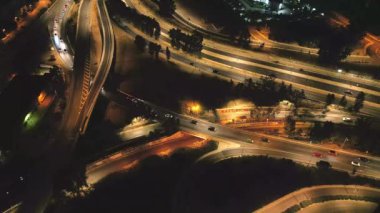 Yoğun bir şehir kavşağı üzerinde gece görüşü, kavis boyunca hareket halindeki araçların parlayan ışıklarını gösteriyor..