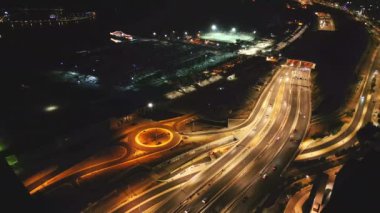 Yoğun bir şehir kavşağı üzerinde gece görüşü, kavis boyunca hareket halindeki araçların parlayan ışıklarını gösteriyor..