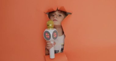Neşeli bir çocuk elinde parlak bir LED mikrofonla portakal renkli bir arka planda yüzünü açıyor. Eğlenceli bir karaoke ya da şarkı söyleme anı öneriyor..