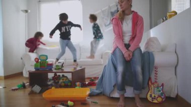 Yorgun anne gözleri kapalı oturur ve kanepeye uzanır. Etrafı oyuncaklarla çevrili, dağınık bir oturma odası, yavaş çekim..