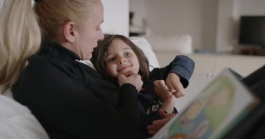 Bir anne küçük oğluna sevgiyle bir kitap okur. Oturma odasının konforunda bir anlığına eğitici bir bağ kurar..