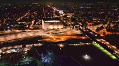 Yoğun bir şehir kavşağı üzerinde gece görüşü, kavis boyunca hareket halindeki araçların parlayan ışıklarını gösteriyor..