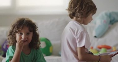 Dijital tabletine dalmış çocuklar güzel ışıklandırılmış bir oturma odasında renkli oyuncaklarla çevrili atıştırmalıklara uzanır..