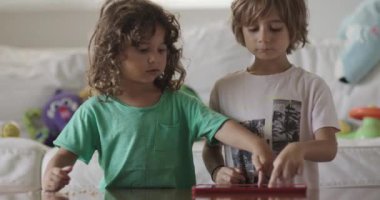 Dijital tabletine dalmış çocuklar güzel ışıklandırılmış bir oturma odasında renkli oyuncaklarla çevrili atıştırmalıklara uzanır..