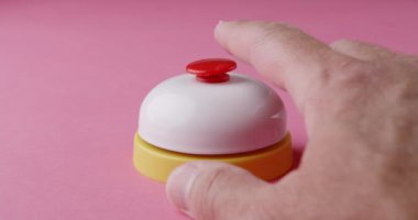 Bir erkeğin parmağı, canlı pembe bir yüzey üzerinde beyaz ve sarı bir zil üzerinde küçük, kırmızı bir düğmeye basar..
