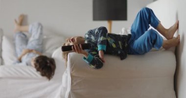 İki çocuk bir oturma odasında aylak aylak yatıyor, biri elinde uzaktan kumandayla kanepede yatıyor, gözleri televizyona yapışık, diğeri yakınlarda oturuyor, uyuşukluk fotoğrafı..