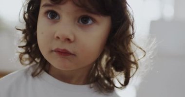 Küçük bir çocuk, uzay temalı bir pijama setiyle evin içinde duruyor, aydınlık bir odada duruyor, rahatlamış, ağlayan.
