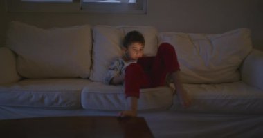 Genç bir çocuk beyaz bir kanepede rahatça oturur. Dikkatini, sakin alacakaranlık saatlerinde elinde tuttuğu kırmızı tablet çeker..