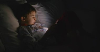 Genç bir çocuk beyaz bir kanepede rahatça oturur. Dikkatini, sakin alacakaranlık saatlerinde elinde tuttuğu kırmızı tablet çeker..